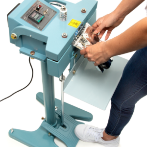 Mujer pisando el pedal del sellador de bolsas de impulso constante azul JORES TECHNOLOGIES®. Está sellando una bolsa de plástico plateada.