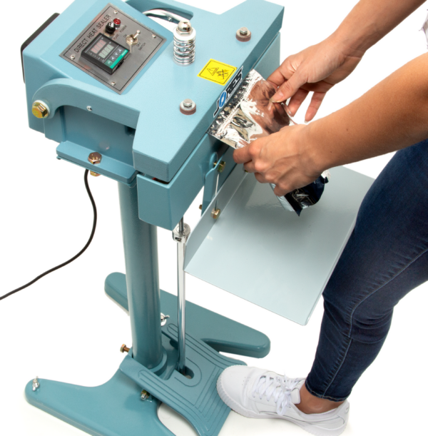 Mujer pisando el pedal del sellador de bolsas de impulso constante azul JORES TECHNOLOGIES®. Está sellando una bolsa de plástico plateada.