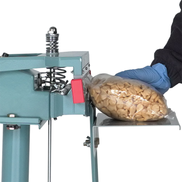 Primer plano de una persona que lleva una camisa larga negra y guantes azules. Está sellando una bolsa grande con galletas de pescado dentro.