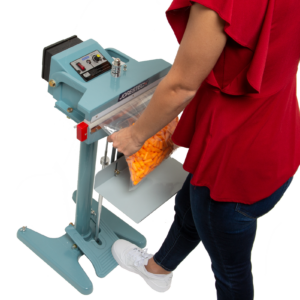 Una persona que lleva una camisa roja y jeans. Está sellando una bolsa grande llena de tapones para los oídos con la selladora de bolsas por impulso de pie de 18 pulgadas.