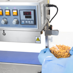 operador con guantes azules insertando una bolsa de plástico llena de galletas saladas naranjas en la guía de la selladora continua de banda de acero inoxidable JORES TECHNOLOGIES®