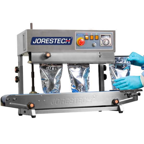 operador con guantes azules introduciendo bolsas de plástico plateadas en la máquina para sellarlas con una selladora continua de banda JORES TECHNOLOGIES®