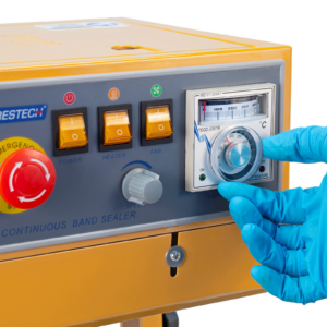 operador con guantes azules ajustando la temperatura en el dial analógico del panel de control de la selladora continua de banda Jorestech