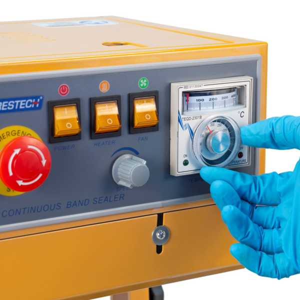 operador con guantes azules ajustando la temperatura en el dial analógico del panel de control de la selladora continua de banda Jorestech