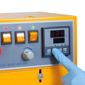 operador con guantes azules ajustando la temperatura en el dial analógico del panel de control de la selladora continua de banda JORES TECHNOLOGIES®