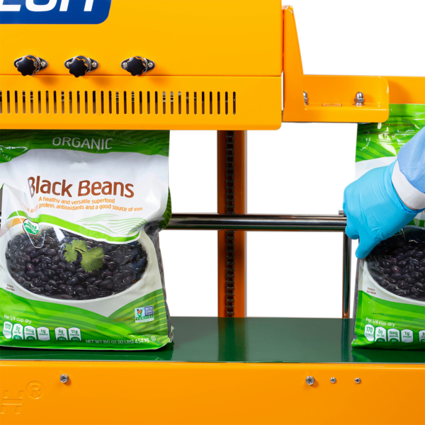 Operador con ropa azul desechable sellando y codificando bolsas grandes de plástico de 10 lb llenas de frijoles negros con una selladora continua de banda vertical JORES TECHNOLOGIES® para sellado vertical