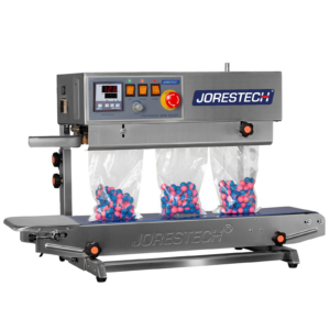 JORES TECHNOLOGIES® selladora continua de banda de acero inoxidable de izquierda a derecha. La selladora vertical de bolsas de sobremesa está sellando una producción de bolsas de plástico llenas de bolitas de pintura azules y rosas.