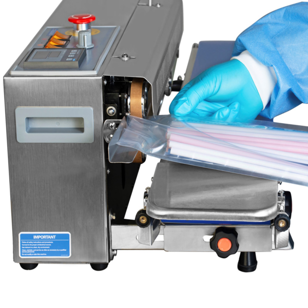 Operario insertando una bolsa transparente llena de pajillas de múltiples colores desde el lado izquierdo de una selladora continua de banda de acero inoxidable JORES TECHNOLOGIES® de izquierda a derecha con panel digital de control de temperatura para sellar la bolsa plástica.