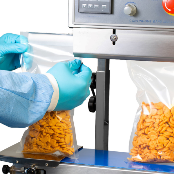 El operador está introduciendo varias bolsas de plástico llenas de galletas por el lado izquierdo de la máquina selladora continua de banda JORES TECHNOLOGIES® para sellar las bolsas.