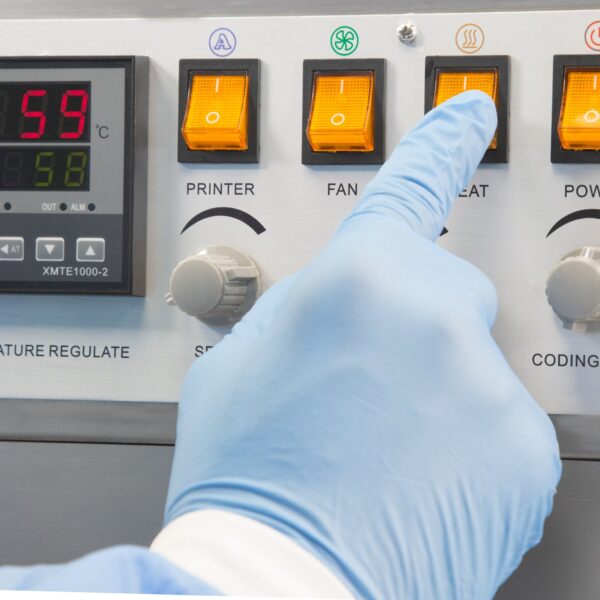Primer plano que muestra el panel de control de una selladora continua de bandas JORES TECHNOLOGIES® y la mano de una persona presionando un interruptor naranja para ajustar la selladora de bolsas y comenzar a sellar bolsas de plástico.