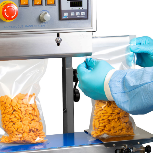 operador insertando varias bolsas de plástico con galletas saladas naranjas en una máquina selladora continua de bolsas JORES TECHNOLOGIES® de acero inoxidable y orientación vertical