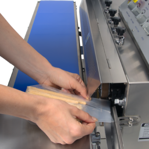 Manos de una persona insertando una bolsa llena de palitos de pan en la cinta de sellado de una selladora continua horizontal digital de acero inoxidable