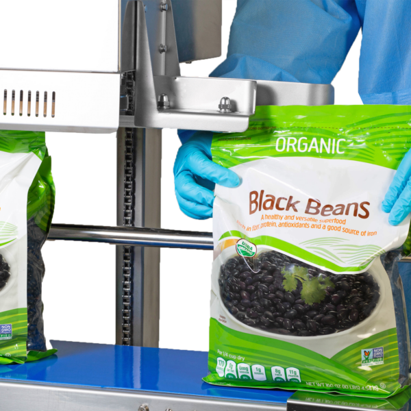 Operario con ropa azul desechable sellando y codificando bolsas plásticas grandes de 10 libras llenas de frijoles negros con una selladora continua vertical JORES TECHNOLOGIES® para sellado vertical