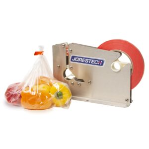 Una selladora manual de bolsas de acero inoxidable con rollo de cinta roja, junto a una bolsa de plástico sellada y llena de pimientos morrones rojos, naranjas y amarillos.
