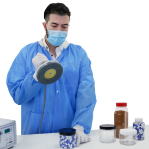 Persona en un laboratorio con equipo de protección personal sellando un frasco de pastillas usando el sellador por inducción Jorestech para protección contra manipulación.