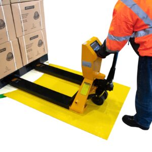 Hombre con chaqueta naranja de alta visibilidad empujando un transpalé cargado con cajas a través de la rampa de carga y hacia la envolvedora de palets.