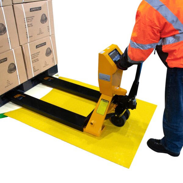 Hombre con chaqueta naranja de alta visibilidad empujando un transpalé cargado con cajas a través de la rampa de carga y hacia la envolvedora de palets.
