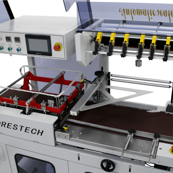 Primer plano que muestra el elemento de sellado, la cinta transportadora motorizada y el panel de control digital de la selladora automática de film térmico en L de color gris claro JORES TECHNOLOGIES®