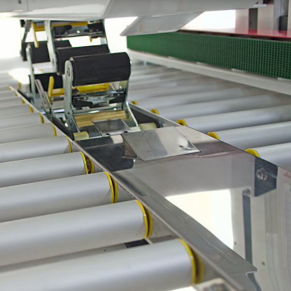 barras rodantes de metal plateado y bandas de tracción verdes en una máquina selladora de cajas con tracción lateral