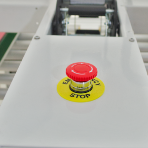 botón rojo de parada de emergencia con etiqueta amarilla en máquina selladora de cajas blanca