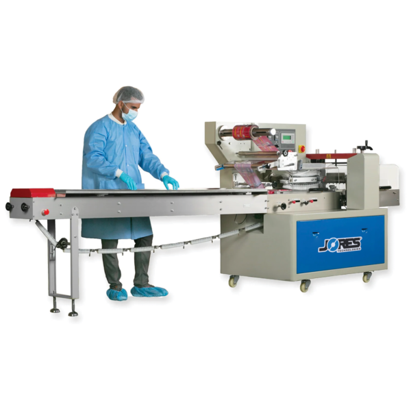 Operador vestido con un traje azul de EPP completo colocando productos sobre la cinta transportadora de cadena de una máquina horizontal de envoltura flow pack de JORES TECHNOLOGIES®