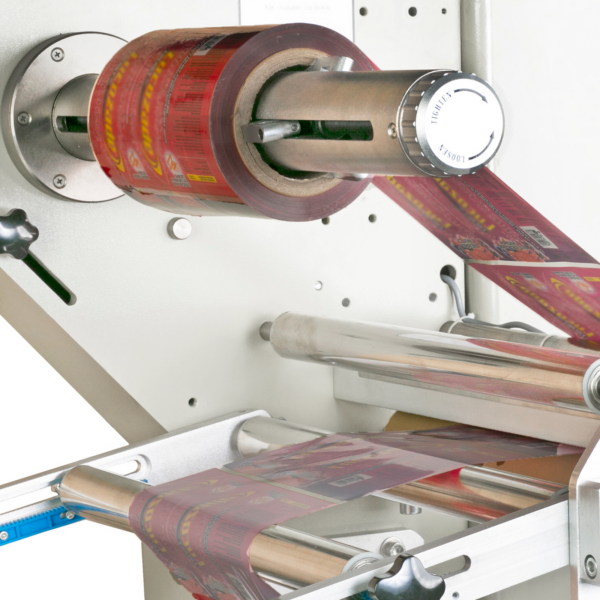 Primer plano del soporte del rollo de film en una máquina flow wrapping, con un rollo de film de embalaje rojo enhebrado a través de la fácil de usar máquina horizontal flow wrapper