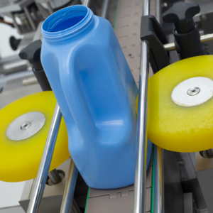 Aplicador automático doble de etiquetas de acero inoxidable con envases ovalados azules de plástico colocados sobre la cinta transportadora. La máquina está colocando las etiquetas adhesivas en un lado de los envases azules.