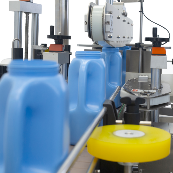 Primer plano que muestra el aplicador automático de etiquetas JORES TECHNOLOGIES® en producción con 5 envases plásticos ovalados azules sobre el transportador integrado a la máquina