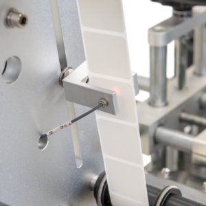 Primer plano del sensor óptico del aplicador automático de etiquetas JORES TECHNOLOGIES® para cajas y contenedores planos
