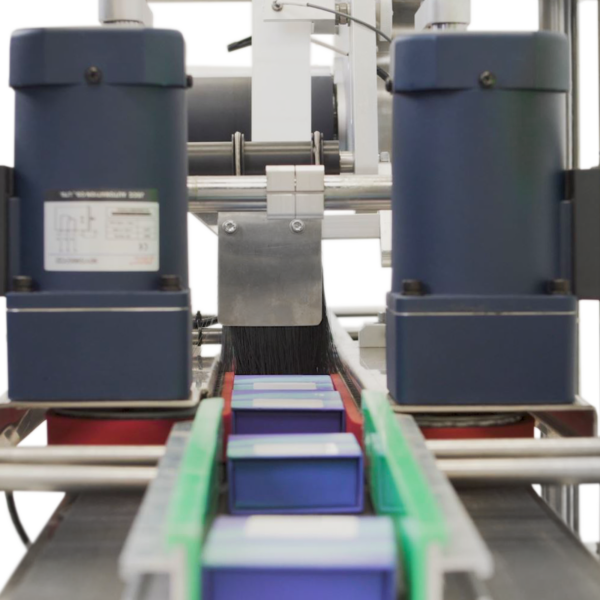 El etiquetador automático en producción aplicando etiquetas sobre la parte superior de pequeñas cajas planas azules colocadas en la cinta transportadora del aplicador automático de etiquetas JORES TECHNOLOGIES®