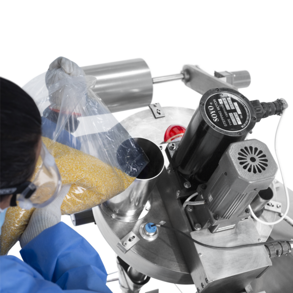 Vista superior de un operador que lleva una bata PPE desechable azul, vaciando un polvo granulada en la tolva de un sistema vertical de formado, llenado y sellado (VFFS)