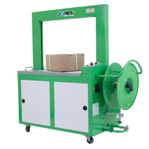 Una máquina automática de flejado de polipropileno JORES TECHNOLOGIES® verde y gris, con un rollo de fleje instalado en el dispensador. La máquina está flejando un artículo de forma cilíndrica