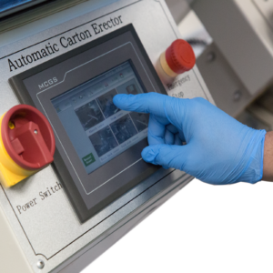 operador con ropa azul ajustando el panel de control digital en una formadora automática de cajas junto a botones y interruptores rojos.