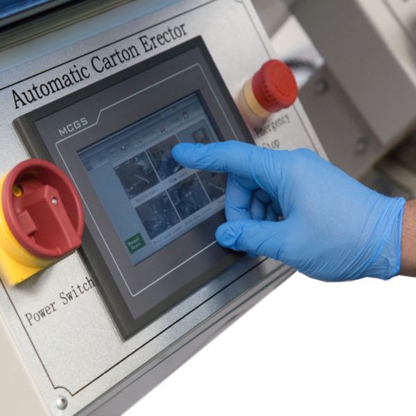 operador con ropa azul ajustando el panel de control digital en una formadora automática de cajas junto a botones y interruptores rojos.