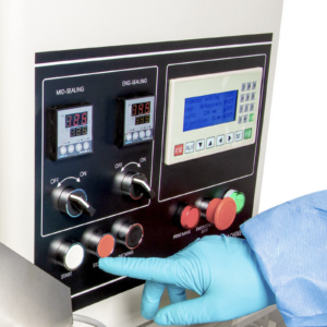 Se ve a un operador con un guante desechable de EPP azul manejando una máquina envasadora horizontal HFFS flow pack. Se muestra el panel de control y está a punto de presionar el botón de inicio.