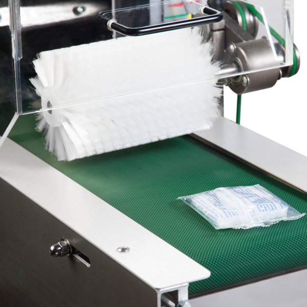 Paquete tipo pillow con un producto en su interior, sobre una cinta transportadora texturizada verde de salida para llevar, después de haber sido sellado por una máquina automática de flow wrap HFFS invertida