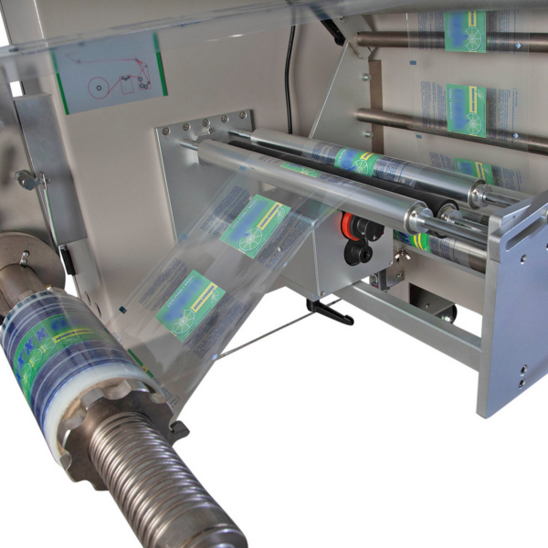 Primer plano del área de envasado y sellado en un sistema flowpack HFFS automático invertido. El soporte del rollo de film está equipado con un rollo de film de embalaje rojo, enhebrado a través de la máquina y listo para usar.