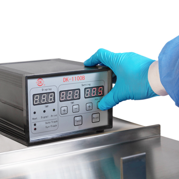 Operador con un guante desechable de EPP azul operando una máquina horizontal HFFS de flow pack. Se muestra el panel de control mientras presiona un botón para realizar ajustes al modo de funcionamiento de la máquina.