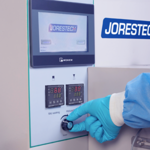 Se ve a un operador con un guante desechable de EPP azul operando una máquina de flow pack horizontal HFFS. Se muestra la pantalla LCD, junto con algunas de las funciones de control de la máquina.