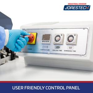Primer plano del panel de control de una máquina de embalaje retráctil tipo cámara JORES TECHNOLOGIES®. Una mano con un guante azul está girando el interruptor de ENCENDIDO / APAGADO. El panel de control muestra controles de temperatura, perillas giratorias de tiempo de sellado y tiempo de retracción. Una franja azul en la parte inferior con letras blancas dice Panel de control fácil de usar.