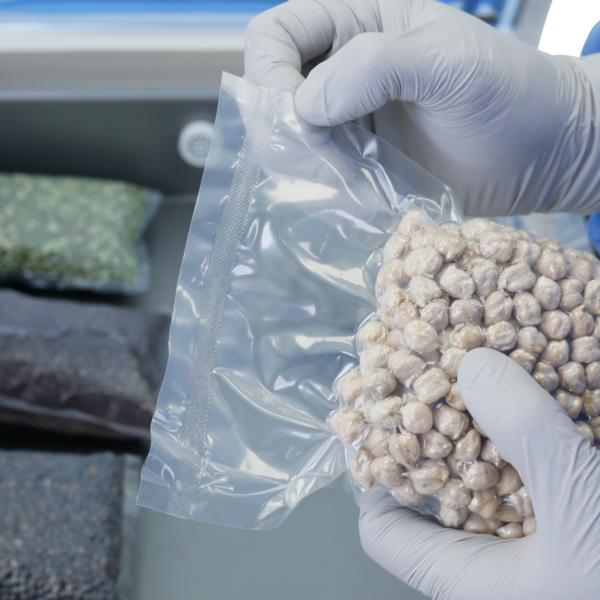 Persona con guantes de nitrilo sosteniendo una bolsa con garbanzos. Está mostrando el sellado realizado por una selladora al vacío comercial de una sola cámara JORES TECHNOLOGIES® con barras de sellado dobles.