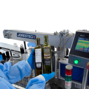 hombre con guantes azules sosteniendo dos botellas verdes de aceite con etiquetas colocadas después de usar el aplicador automático dual de etiquetas JORES TECHNOLOGIES® para envases planos y redondos, mostrado al fondo