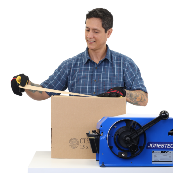 Persona colocando la cinta de papel kraft engomada húmeda sobre una caja de cartón marrón después de haber sido dispensada por el dispensador de cinta de papel azul JORES TECHNOLOGIES® colocado sobre la misma mesa de trabajo