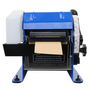 Primer plano del dispensador de cinta engomada JORES TECHNOLOGIES® mostrando el recipiente de agua blanco a la izquierda, la salida de la cinta de papel kraft en el centro y la rueda para ajustar el tamaño de la cinta en el lado derecho de la máquina
