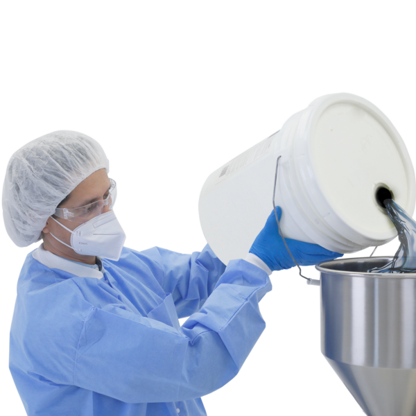 Un trabajador vestido con EPP y guantes de nitrilo llenando la tolva de una llenadora de pasta de alta viscosidad de sobremesa con pistón de JORES TECHNOLOGIES®
