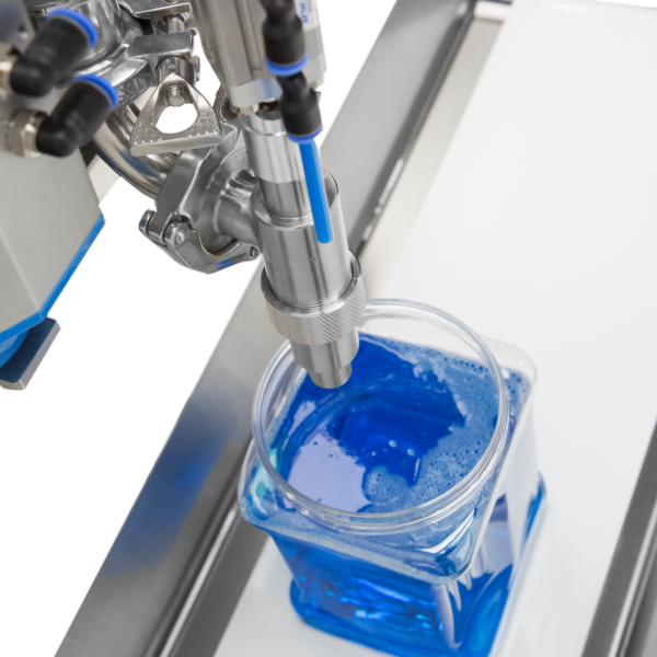 Primer plano de la boquilla del llenador de pasta de pistón. Hay un recipiente transparente que ha sido llenado con líquido azul junto con la máquina