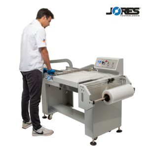 Hombre con guantes azules sellando film retráctil alrededor de una caja con una máquina selladora en L semiautomática JORES TECHNOLOGIES®.