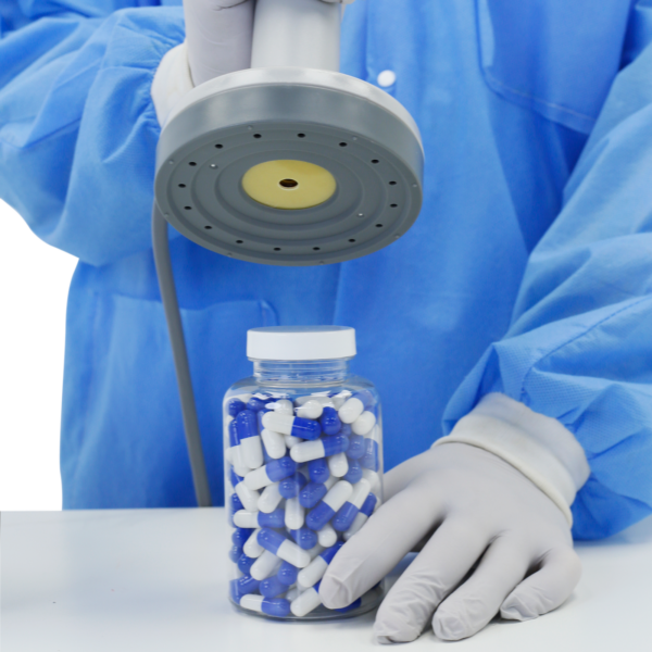 Persona en un laboratorio con equipo de protección personal sellando un frasco de pastillas con la selladora por inducción de tapas Jorestech