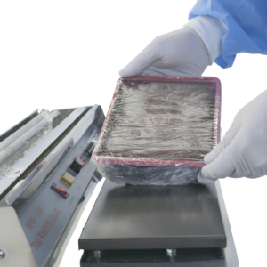 operador con guantes blancos envolviendo una bandeja de alimentos con film retráctil usando una envolvedora manual de bandejas