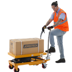 Un hombre que lleva un chaleco de alta visibilidad naranja está presionando el pedal de la mesa elevadora de tijera JORES TECHNOLOGIES® para levantar una caja pesada con facilidad